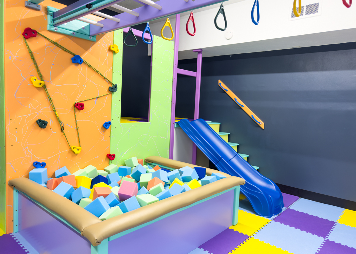 Climbing wall, foam pit, and blue slide inside the sensory gym